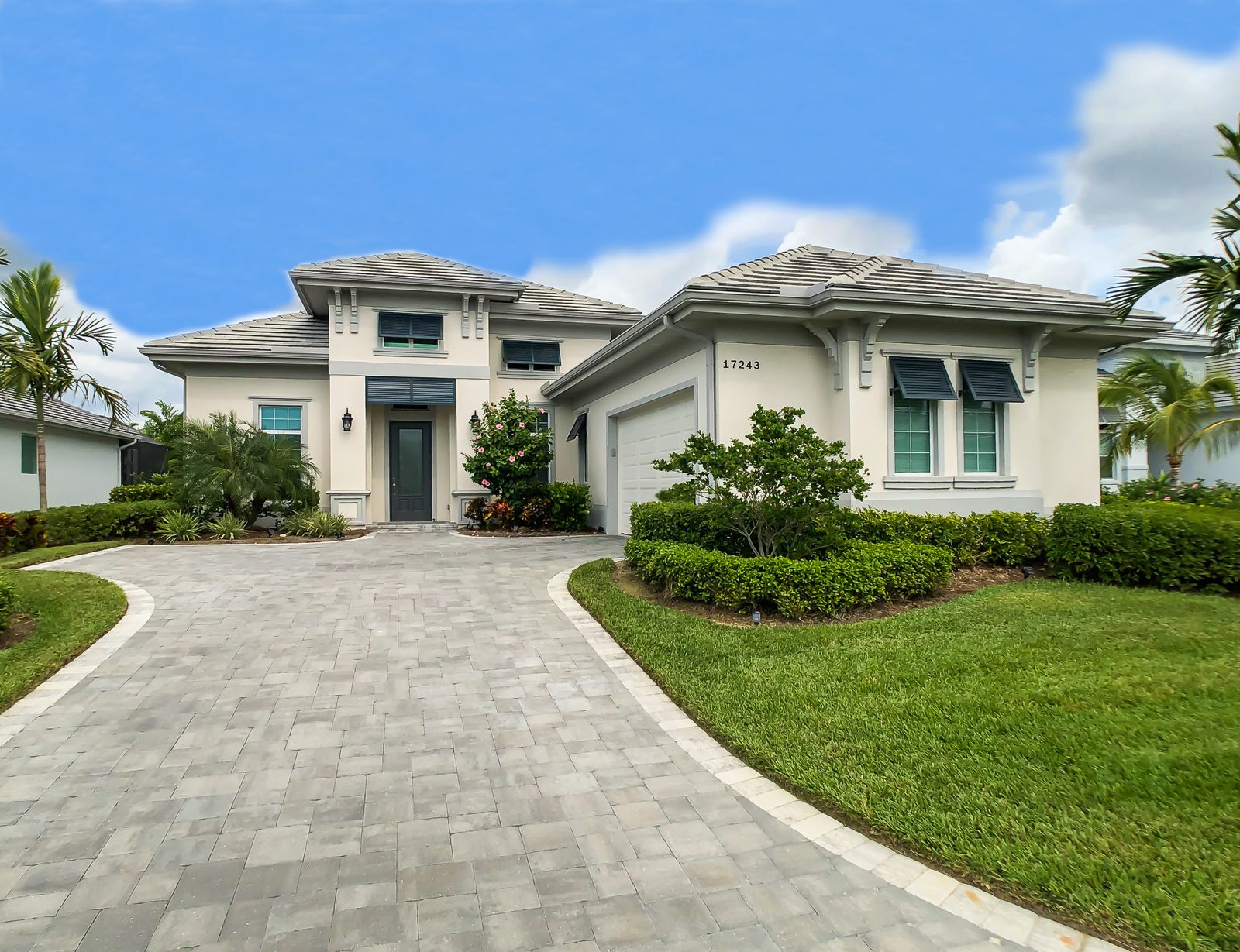 Move-in ready Florida home with a paver driveway, palm trees, and lush landscaping in Lehigh Acres