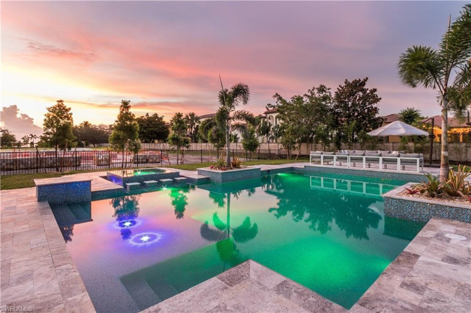 Backyard pool at dusk in Lehigh Acres with palm trees and a pink Florida sky
